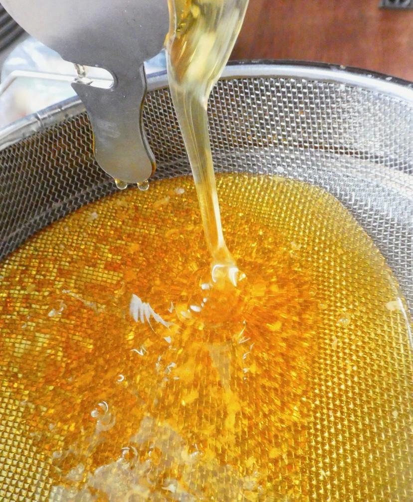 Frisch geschleuderter Honig läuft golden durch ein Sieb der Imkerei Fritschler